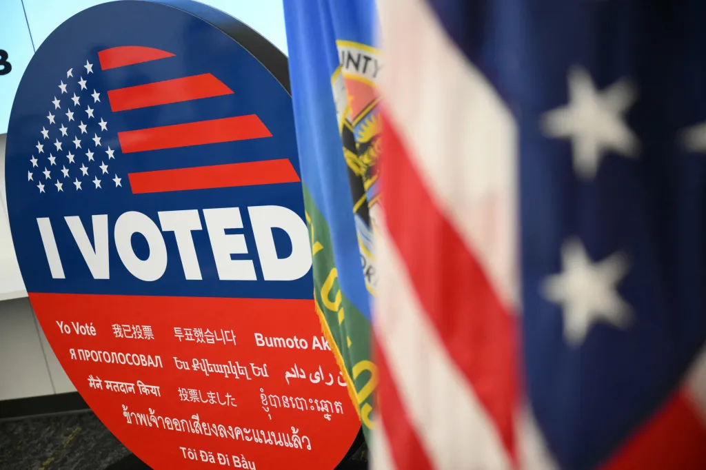 An "I Voted" sign in English and other languages, displayed next to a U.S. flag and another flag.