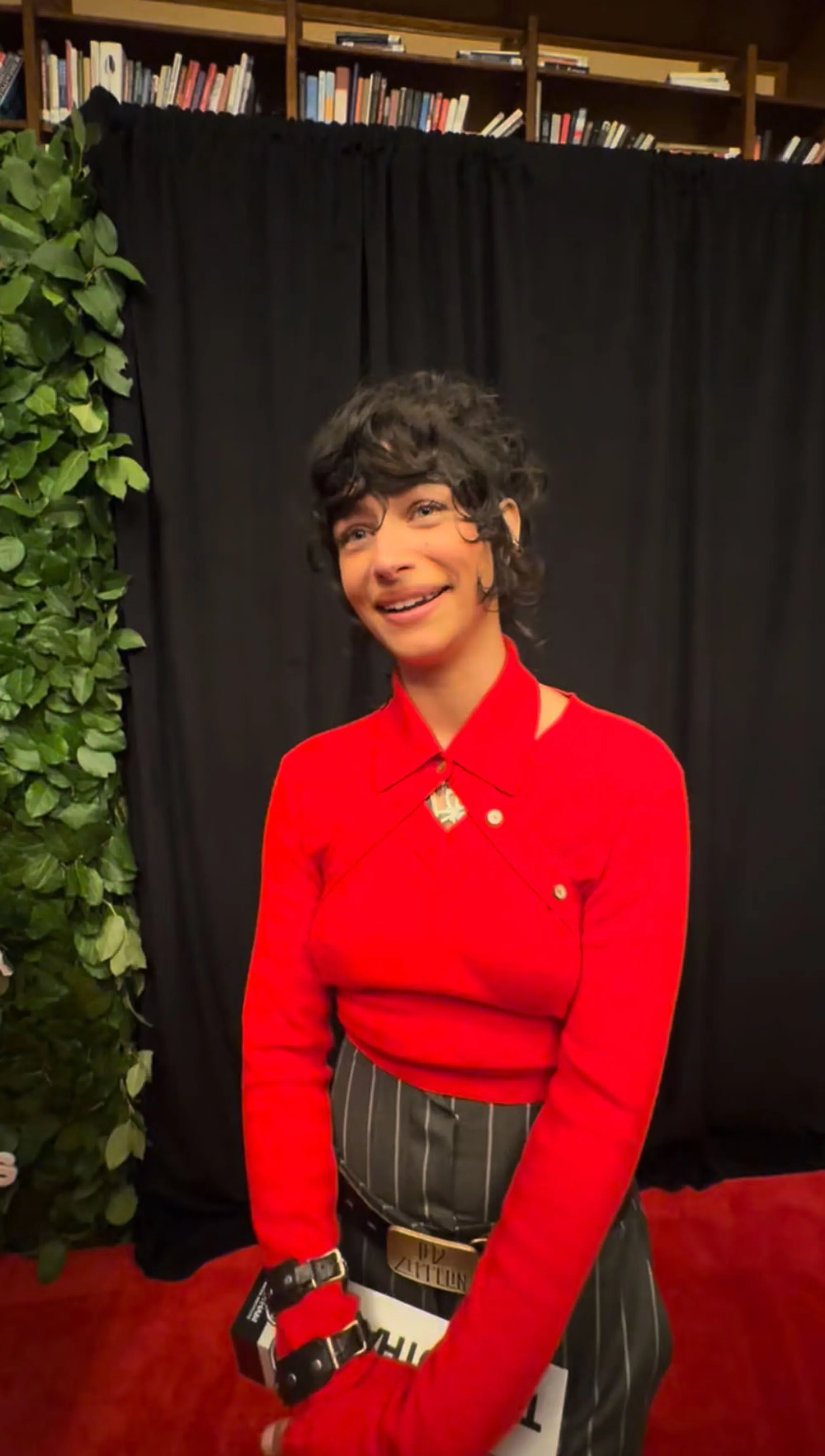 Odessa A'zion smiling in a red shirt and striped pants at the 2026 Gotham TV Awards.