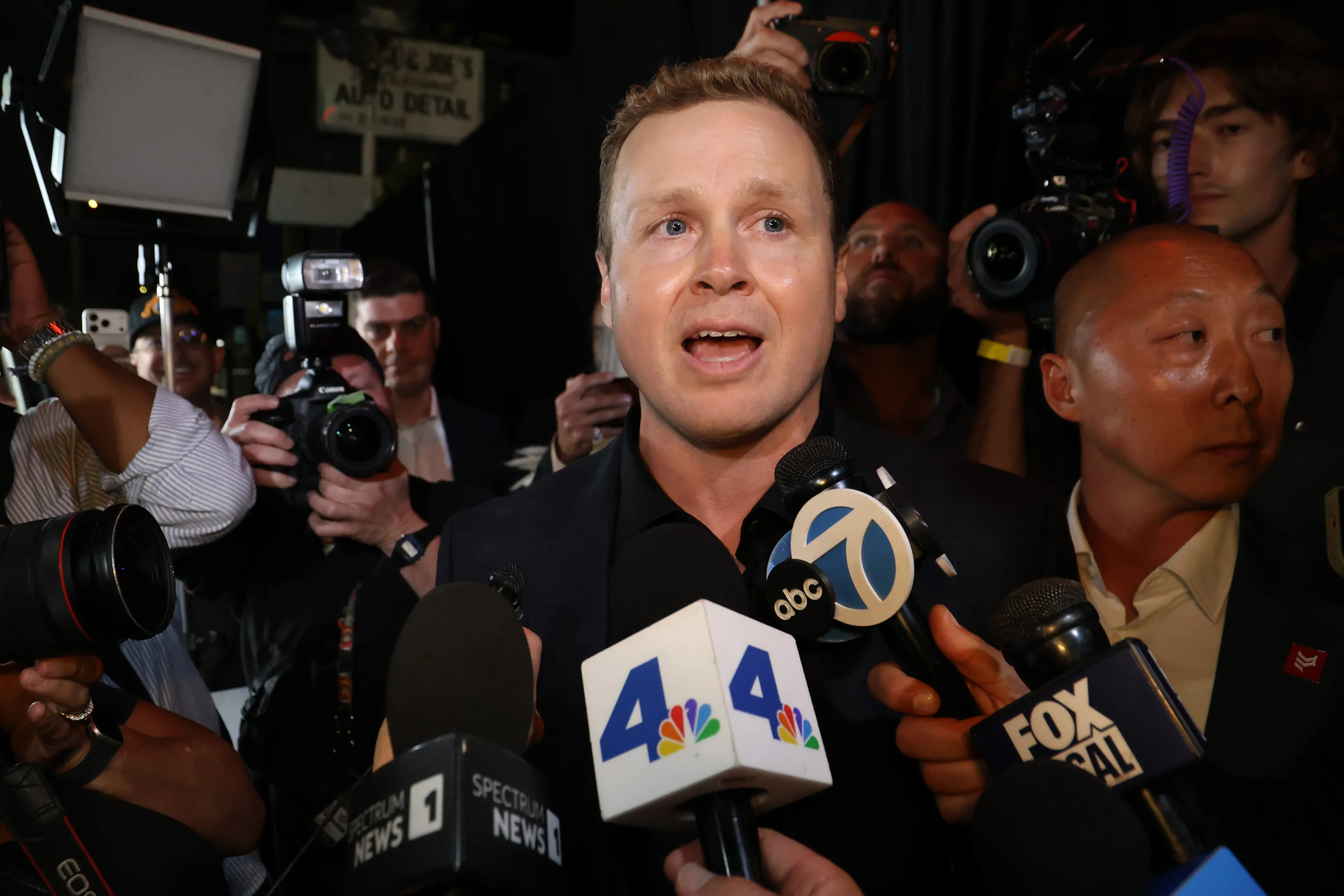 Spencer Pratt speaking into microphones from various news outlets surrounded by paparazzi.
