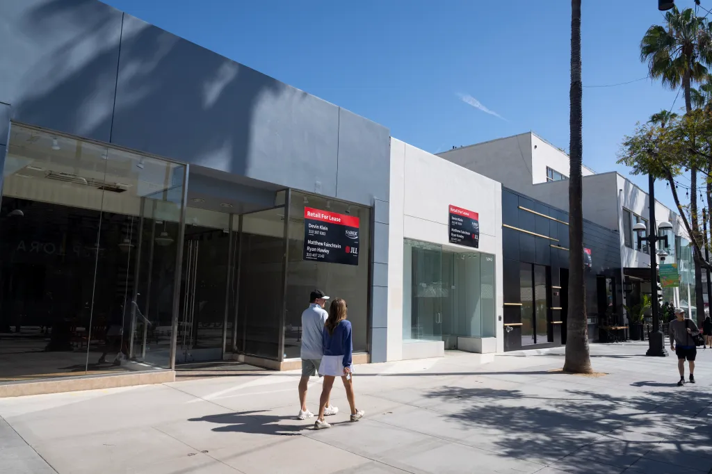 People walk past multiple empty retail spaces with "Retail For Lease" signs in Santa Monica, California.