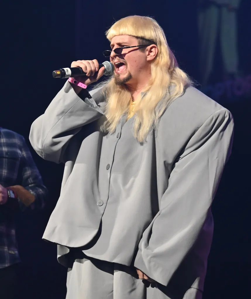 Oliver Tree performing with a microphone in an oversized gray suit.