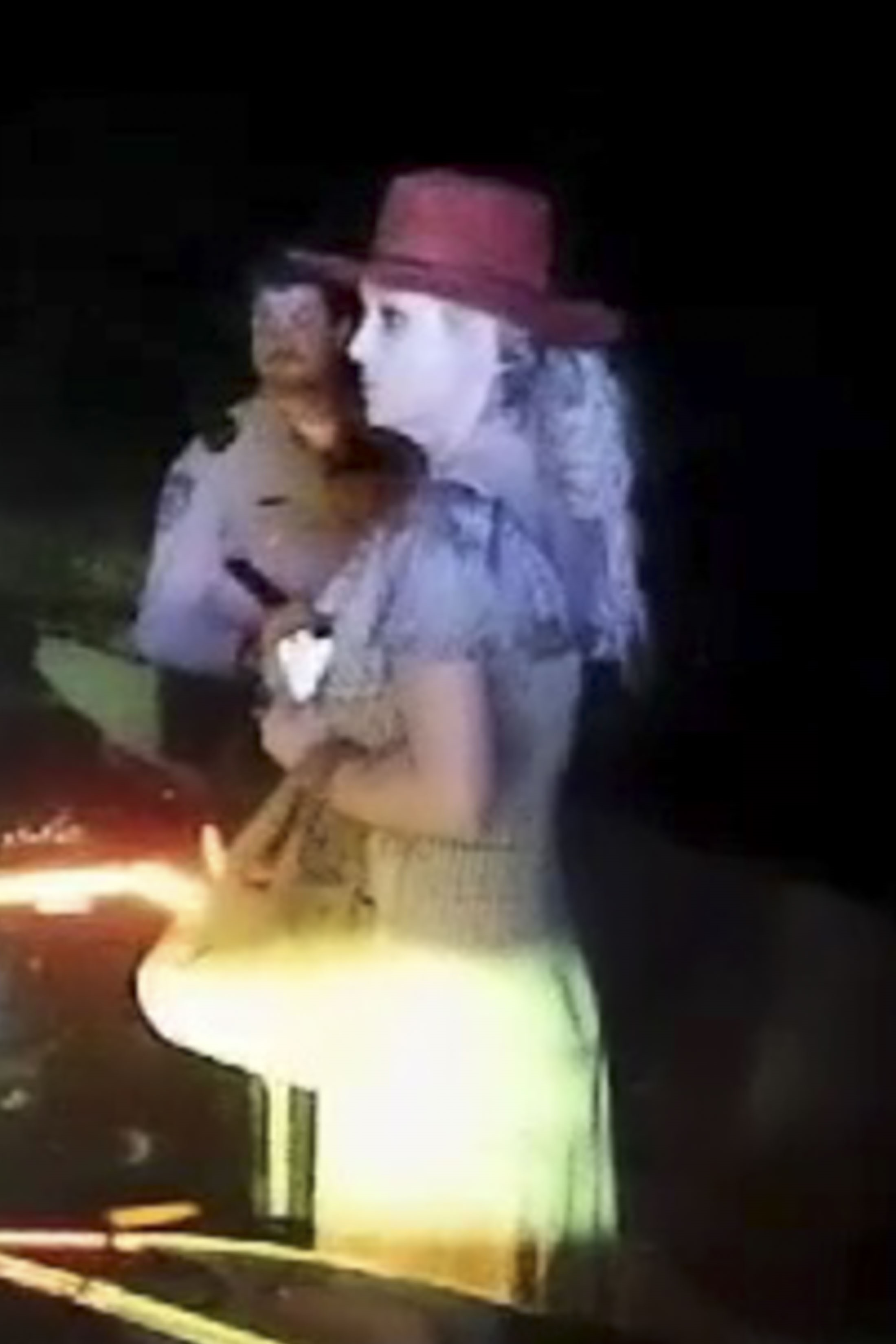 Britney Spears next to a police officer at night with a flashlight beam illuminating her.
