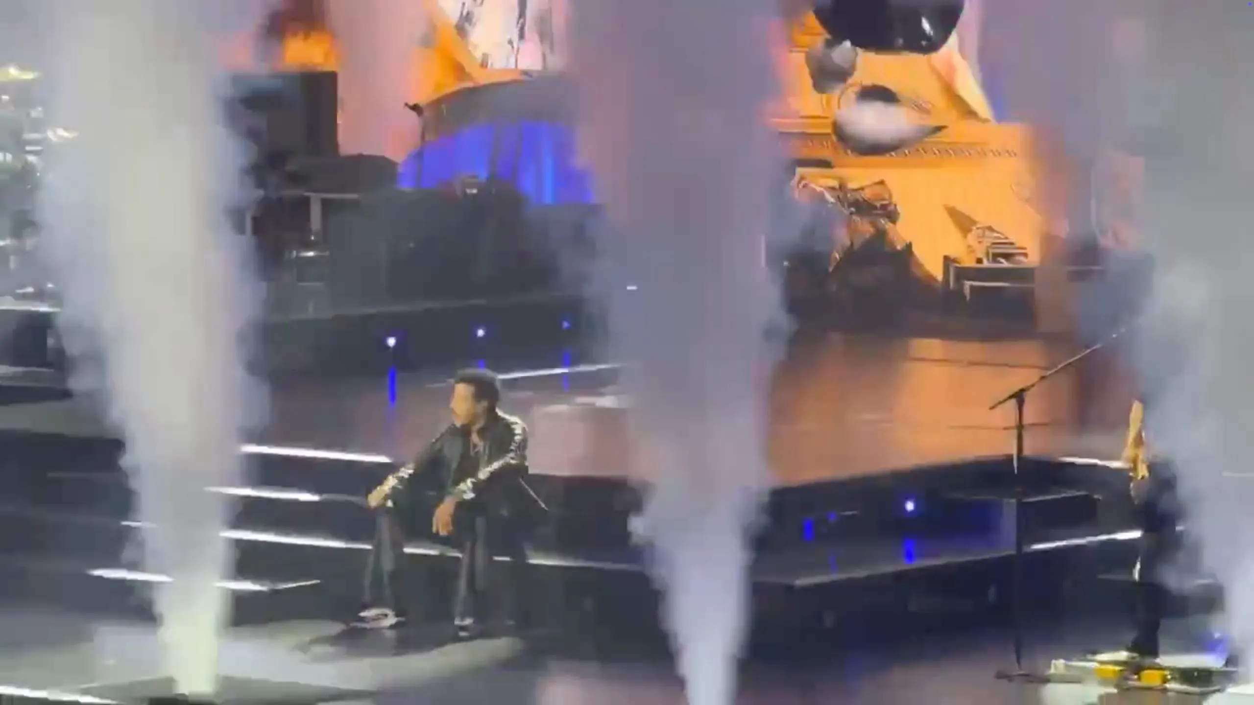 Lionel Richie sits on stage steps, surrounded by smoke, during a concert.