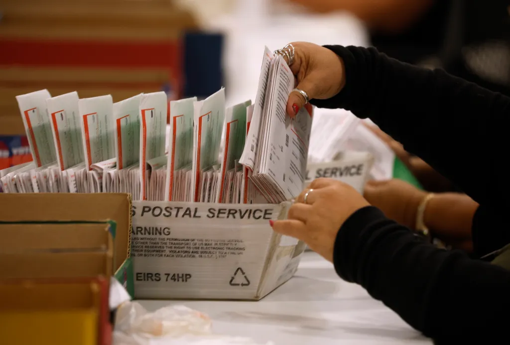A pair of hands sorting through a box of mail-in ballots.