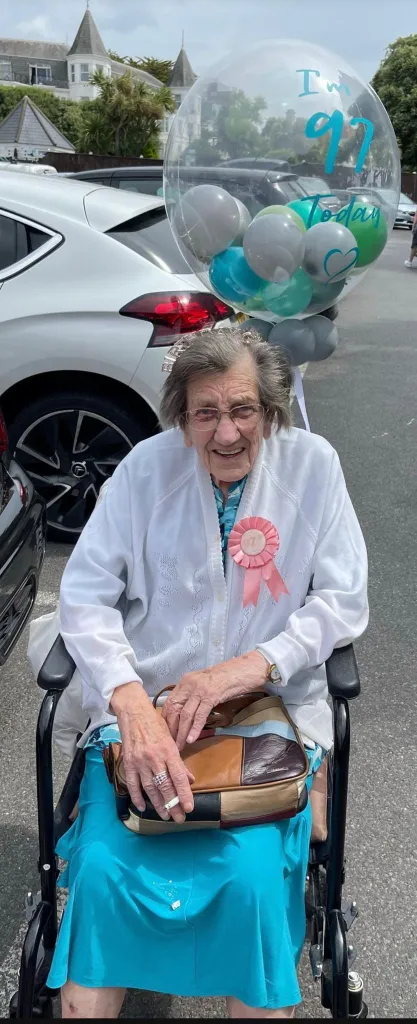 Margaret Ham, 99, holds a cigarette, wearing a tiara and a pink ribbon badge.