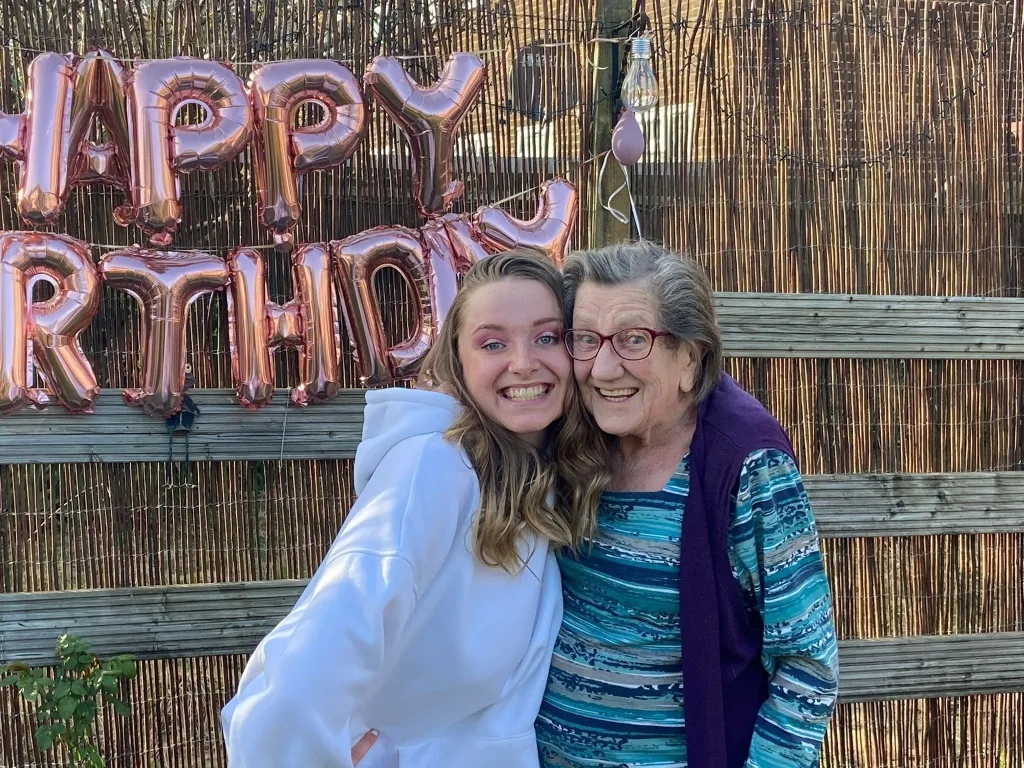 Margaret Ham with her great-granddaughter Megan, posing in front of "Happy Birthday" balloons.