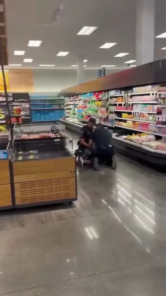 Police apprehending a man in the middle of a grocery store aisle.