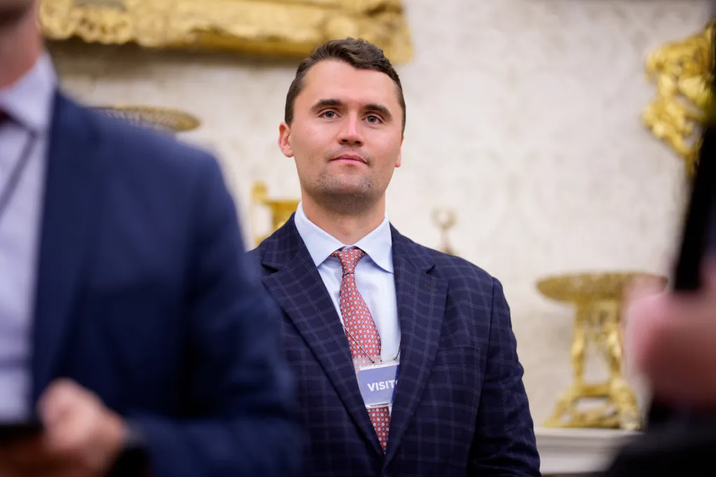 A man in a suit and tie, wearing a "VISITOR" badge, looks forward.