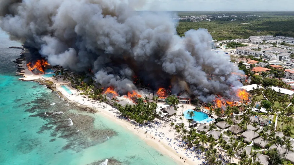 Aerial view of a resort in the Dominican Republic with multiple buildings engulfed in flames and dense black smoke rising into the sky.