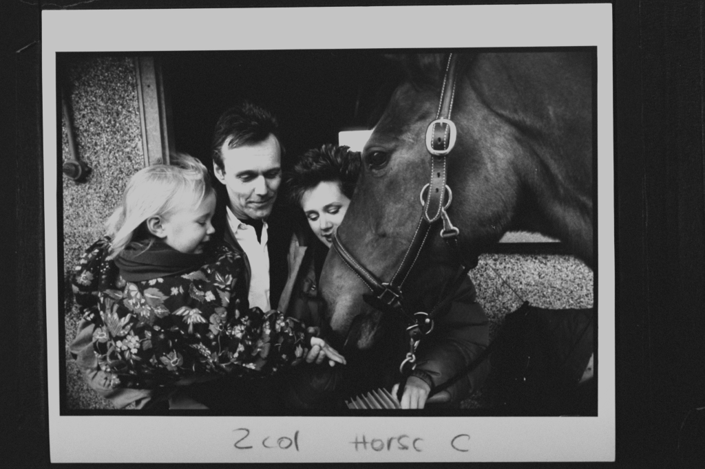 Actor Anthony Head, Sarah Fisher, and their daughter Emily petting a horse at a stable.