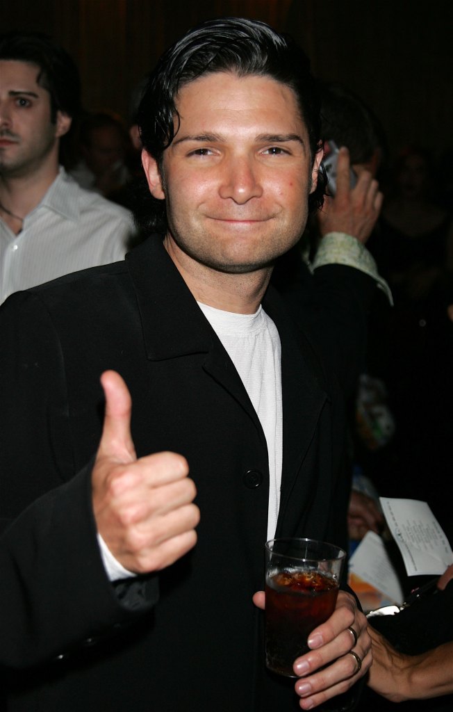 Corey Feldman smiling at an after-party, holding a drink and giving a thumbs up.