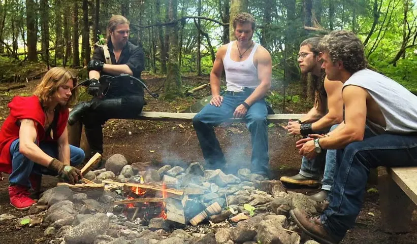 Five men of the Alaskan Bush People series around a campfire in the woods.