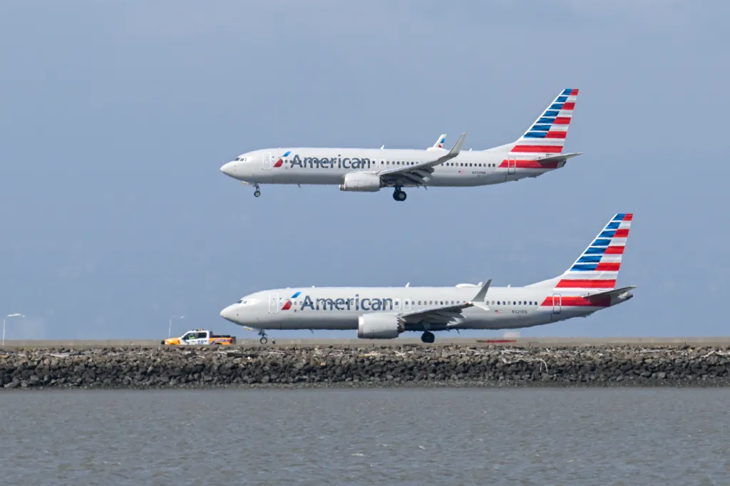 An American Airlines plane in the air above another American Airlines plane on the tarmac at San Francisco International Airport (SFO).