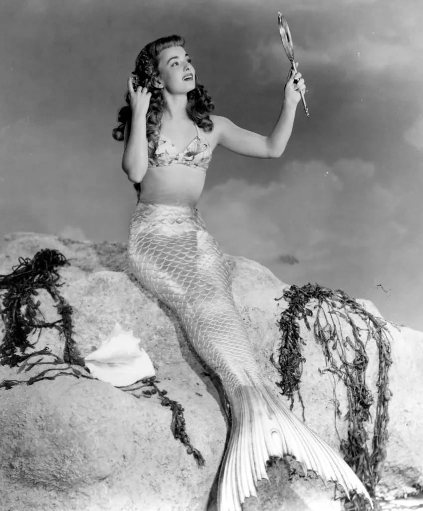 Ann Blyth as a mermaid, adjusting her hair with one hand and holding a mirror with the other, on a rock in "Mr. Peabody and the Mermaid."