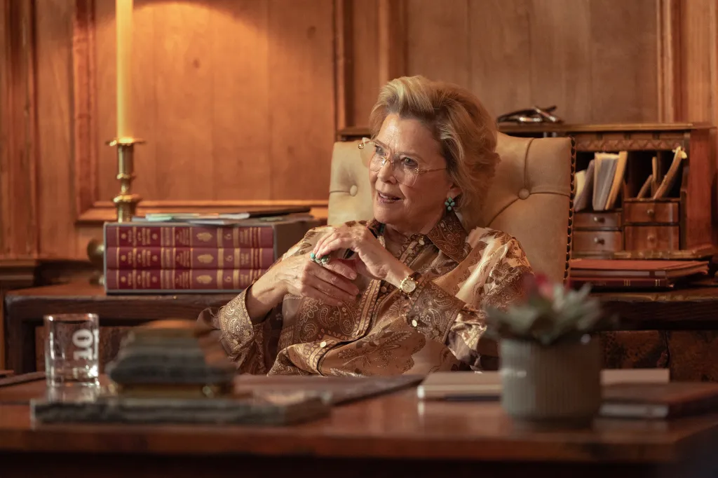 Annette Bening as Beulah Jackson, seated in a high-backed leather chair, wearing a patterned gold blouse, glasses, and a large turquoise ring.