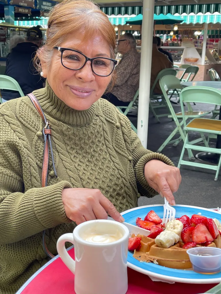 Arabelia Martinez in glasses and a green sweater, eating waffles with fruit.