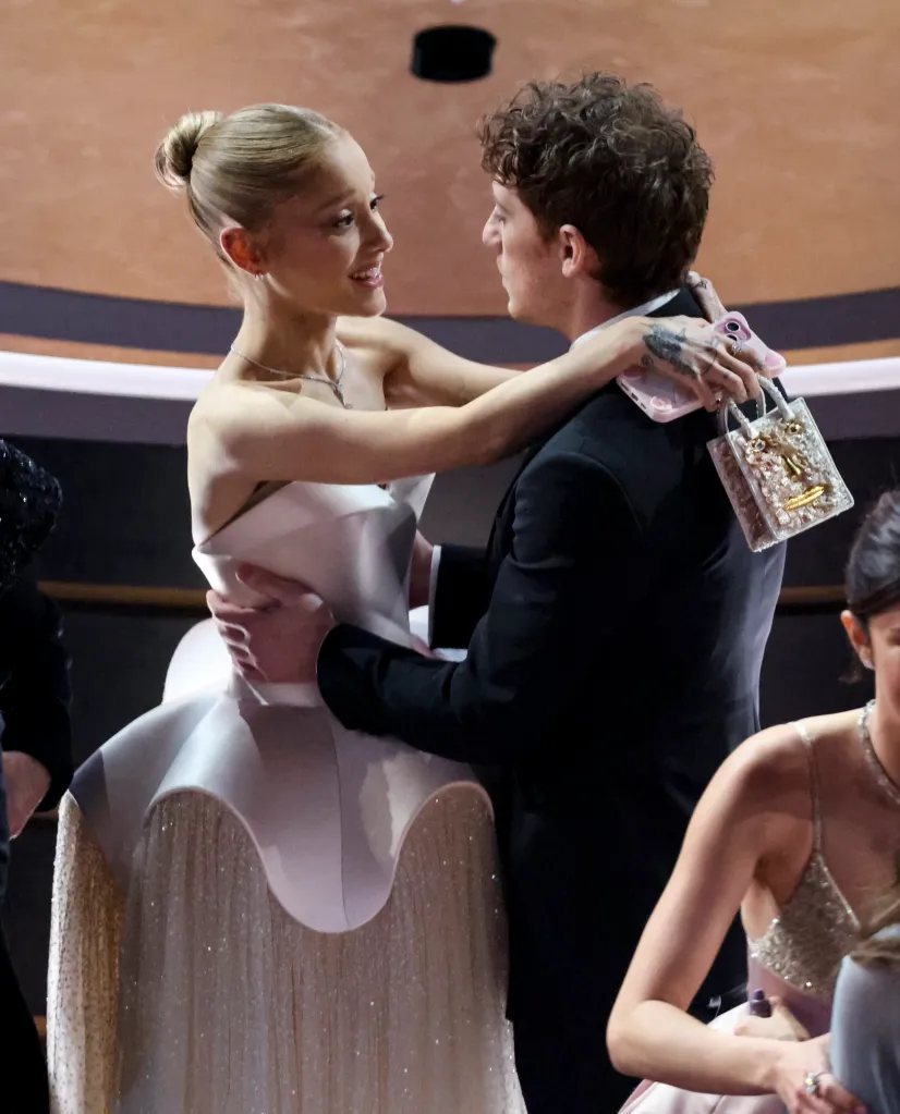 Ariana Grande in a white strapless gown hugging Ethan Slater in a black suit at the 97th Oscars.