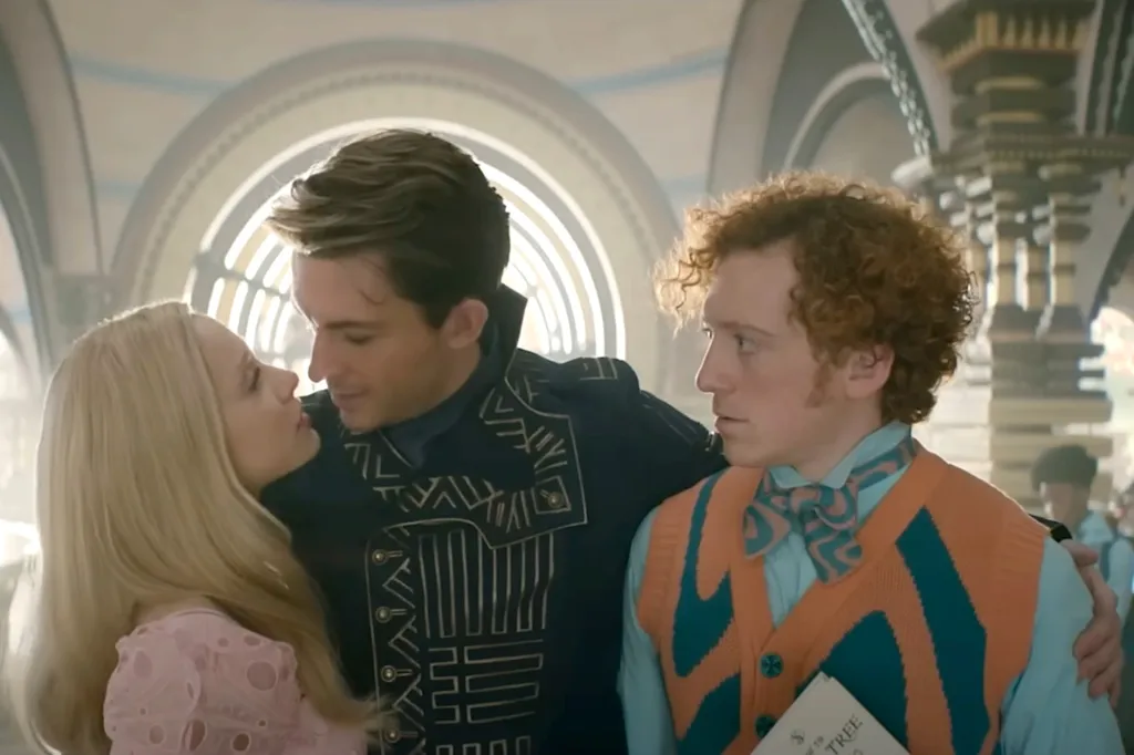 Ariana Grande, in a pink dress,Jonathan Bailey, in a black and white shirt, and Ethan Slater in an orange and green vest, and green shirt and orange and green tie, in a scene from the film "Wicked."