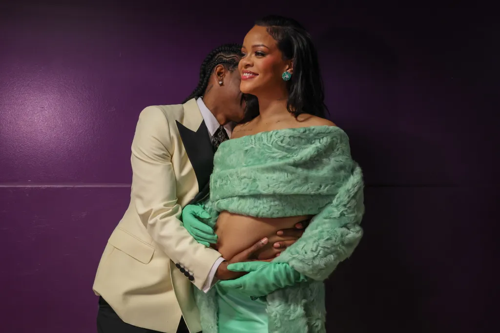 ASAP Rocky with his arm around a smiling Rihanna, who wears a light green fur shawl and green gloves, revealing her pregnant belly.