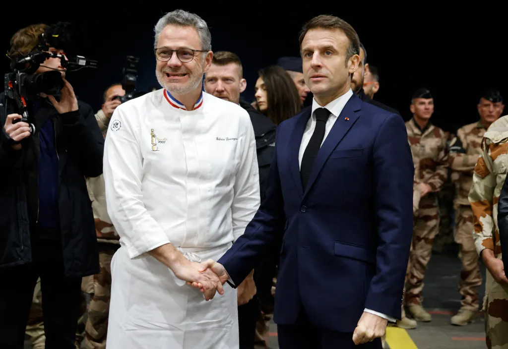French President Emmanuel Macron shaking hands with Chef Fabrice Desvignes during a Christmas dinner event with French forces.