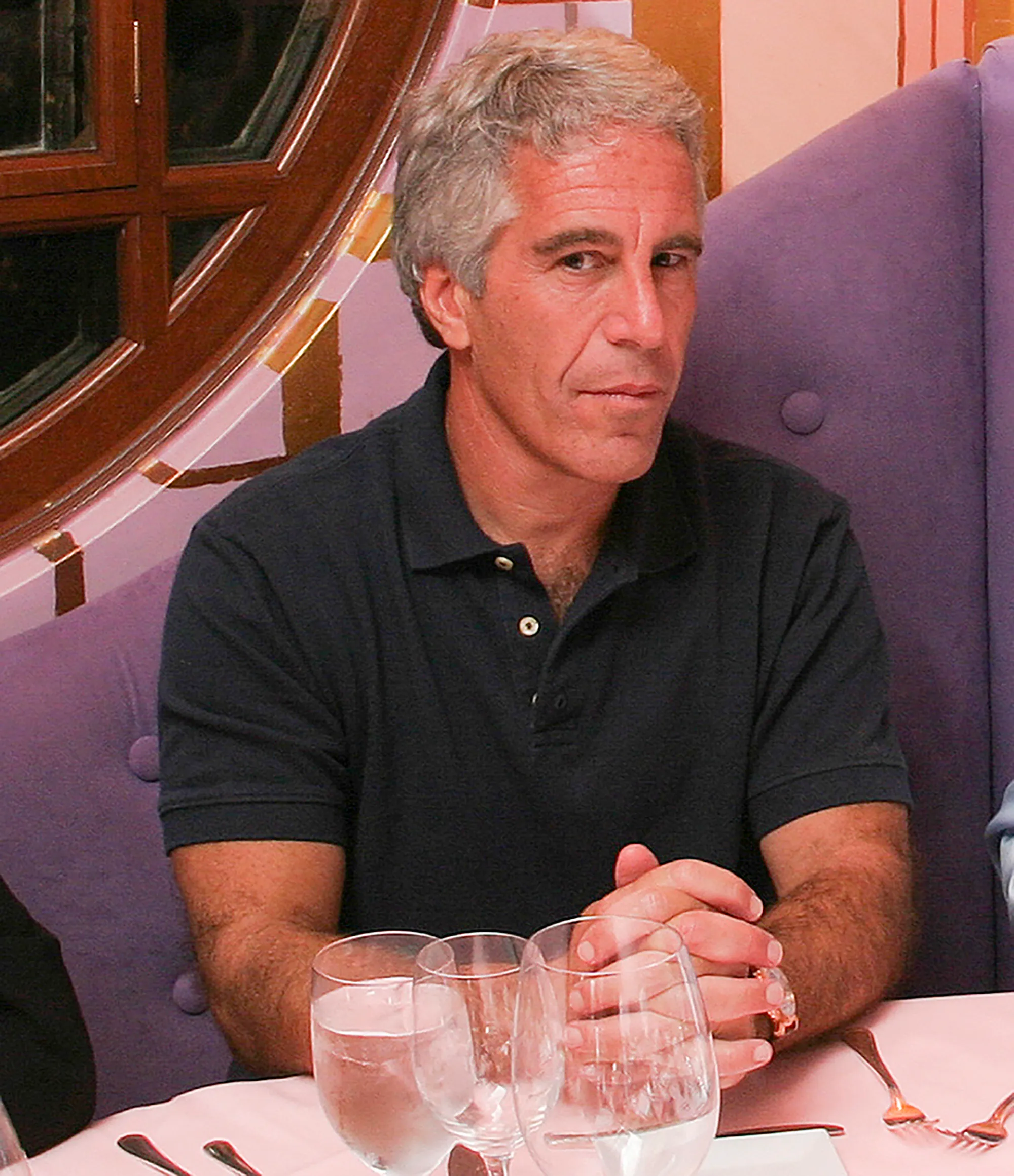 Jeffrey Epstein sitting at a table in a dark polo shirt.