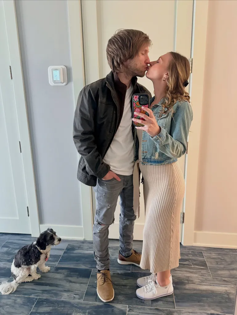 Jesse and Ashley Ridgway sharing a kiss while their dog sits nearby.