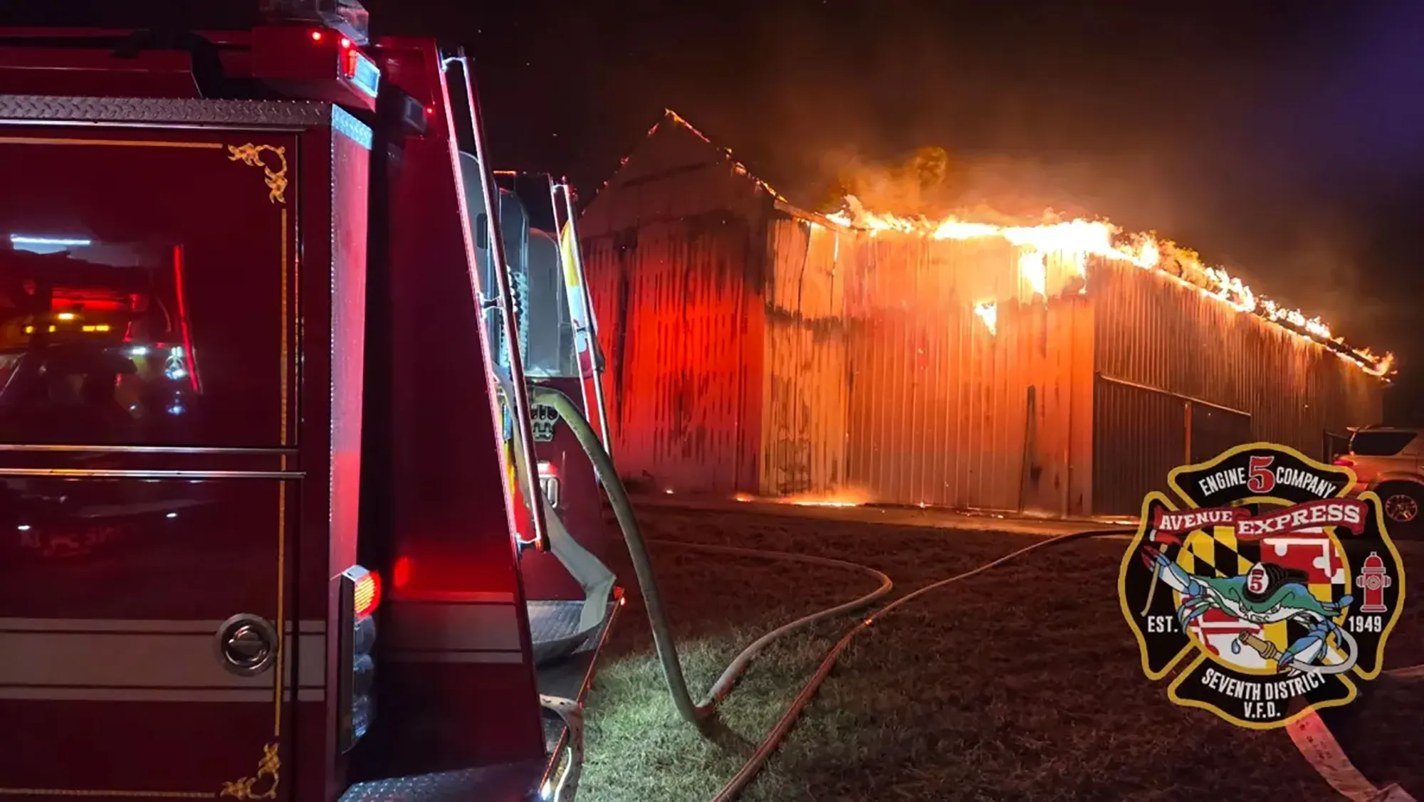 A red fire truck with hoses extended to a burning barn at night.