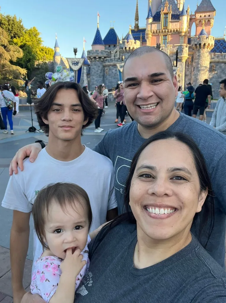 Brianna Nichole, Lt Colonel Gabriel Estrella, Elijah Lepper, and their daughter smiling at a Disney theme park.