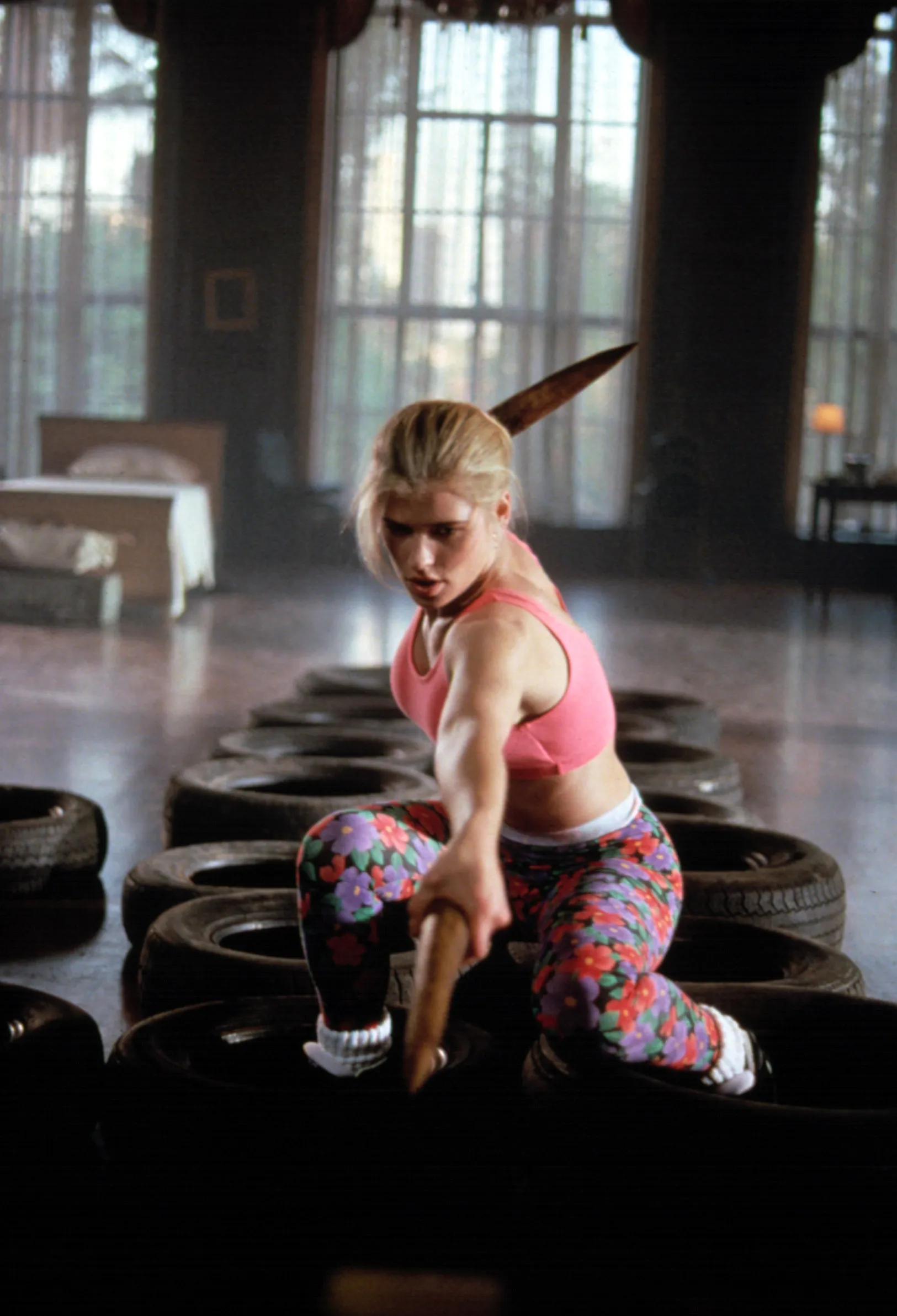 Kristy Swanson holding a wooden stake and kneeling among tires, training for her role in "Buffy the Vampire Slayer."