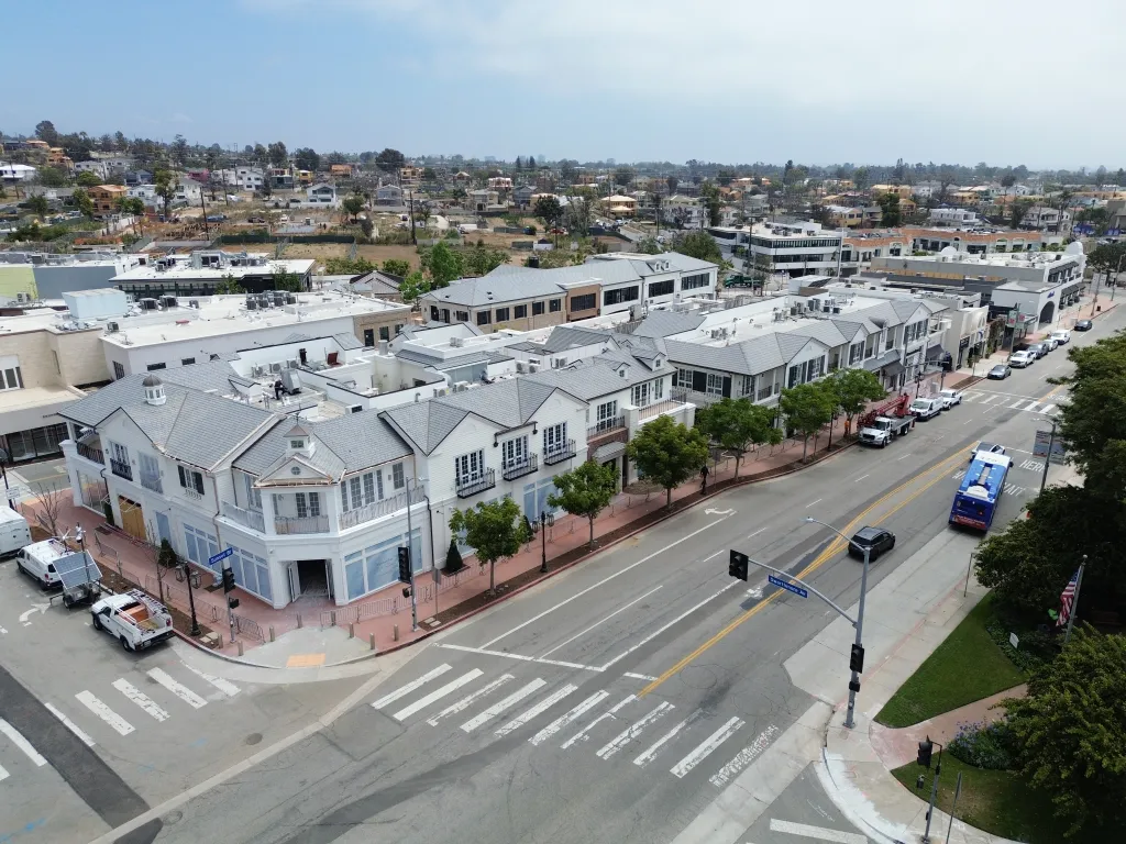 Aerial view of Palisades Village, a street lined with white two-story buildings, cars, and trees.