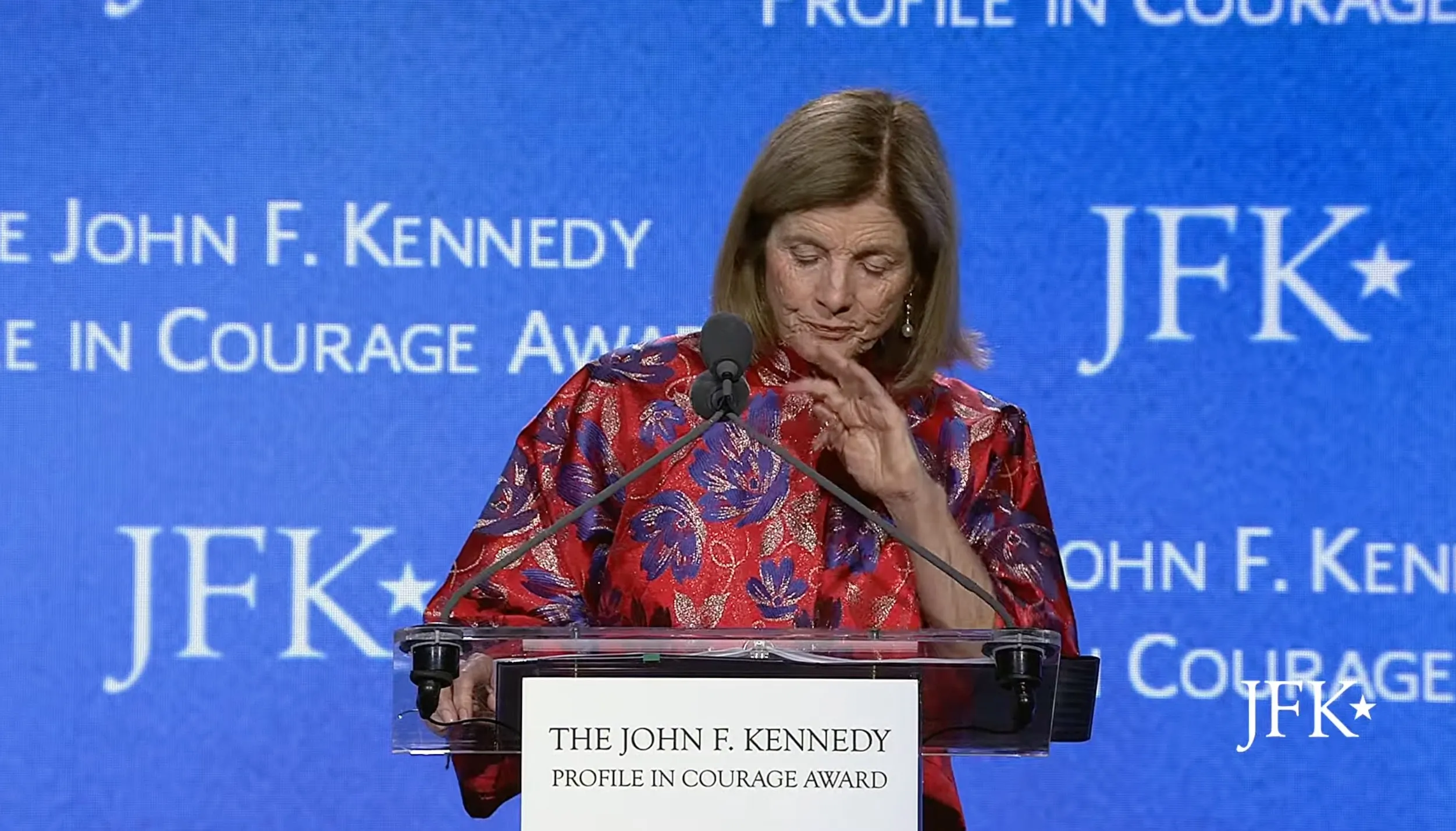 Caroline Kennedy looking tearful at a podium with a blue background featuring the JFK Profile in Courage Award logo.
