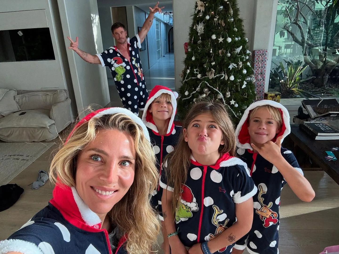 Elsa Pataky takes a selfie with her three children and Chris Hemsworth in festive Grinch pajamas in front of a Christmas tree.