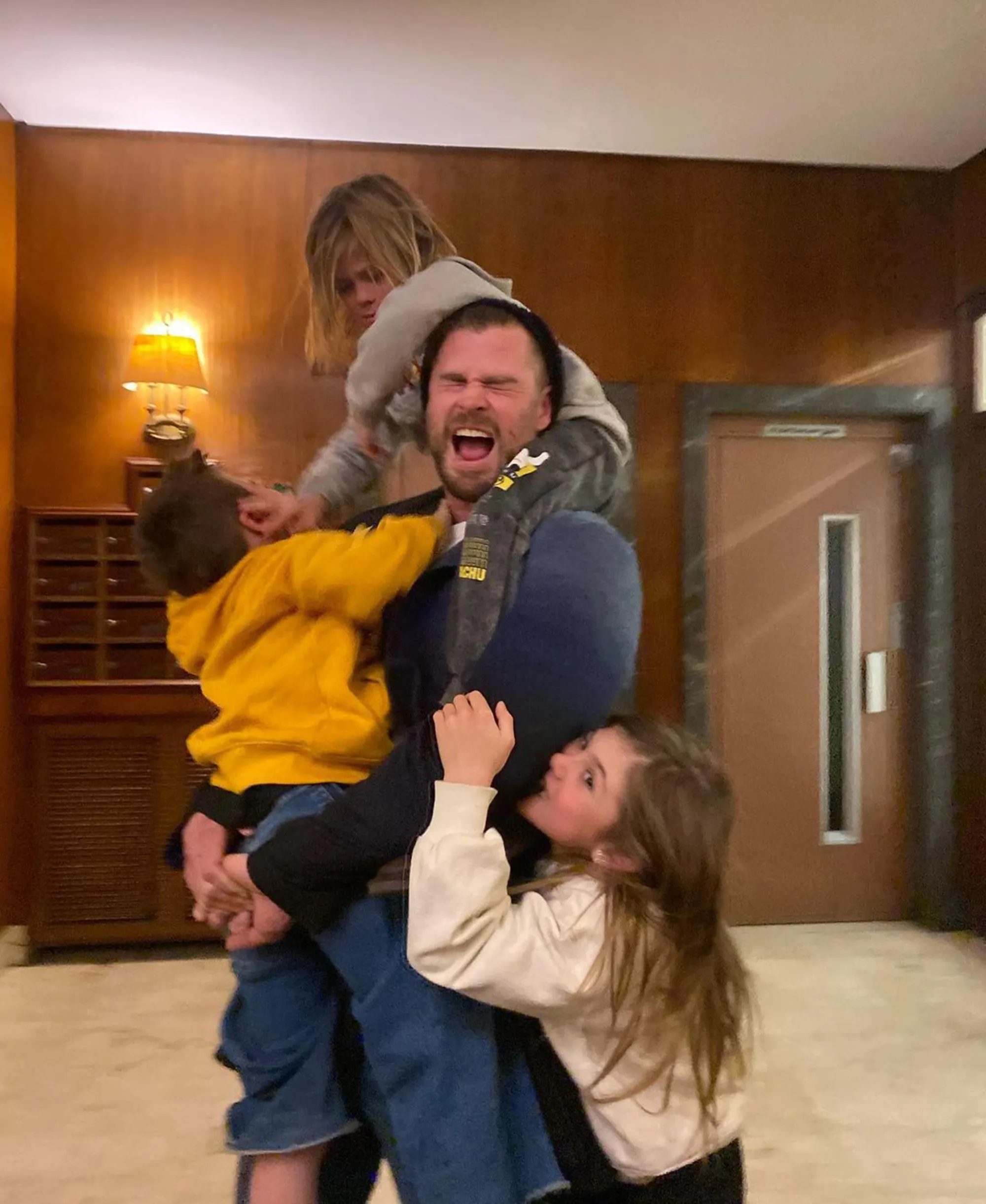 Chris Hemsworth with his three children, two boys and a girl, all climbing on him.