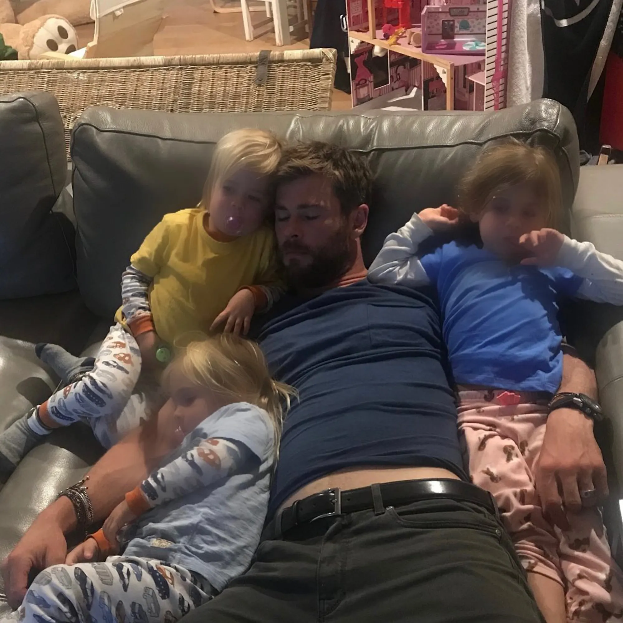 Chris Hemsworth napping on a couch surrounded by his three young children.