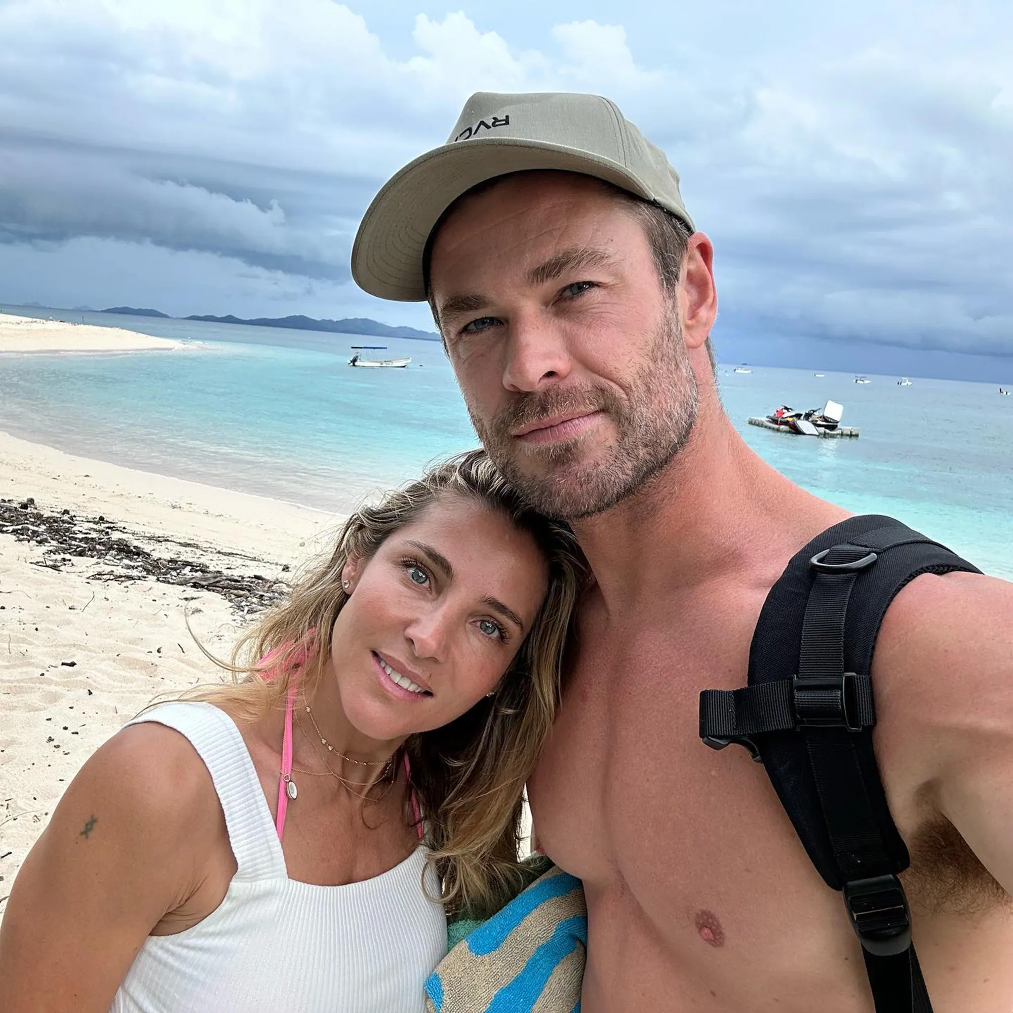 Chris Hemsworth and Elsa Pataky posing for a selfie on a beach with boats in the background.