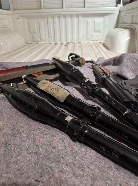 Firearms and RPGs, one with "Bisaam Shahzad Ghafoor" written in Arabic, lying in the back of a truck.
