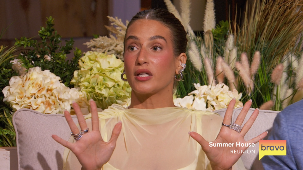 Ciara Miller speaking, gesturing with her hands, wearing large earrings and a sheer yellow top.