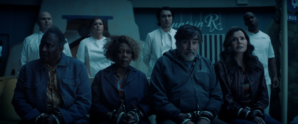 Clarke Peters as Art, Alfre Woodard as Judy, Alfred Molina as Sam, and Geena Davis as Renee, are seated with their hands restrained, while three people in white uniforms stand behind them.