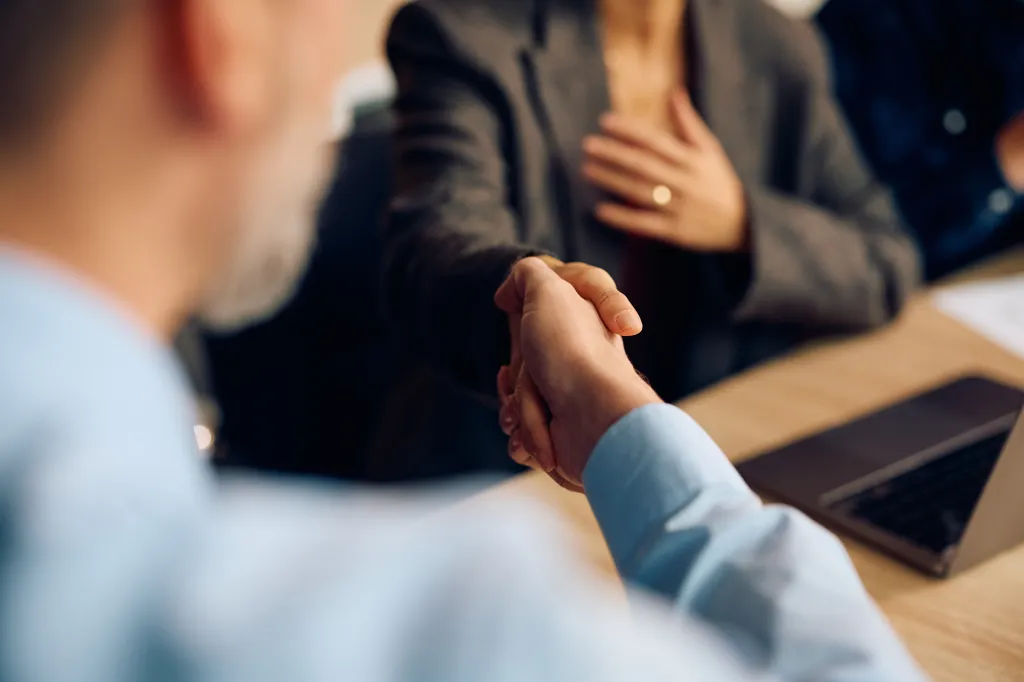 Two business people shake hands across a table.
