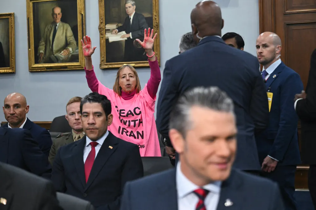 Code Pink protestor Medea Benjamin in a pink t-shirt with "PEACE WITH IRAN" on it, raising her hands with red paint on them.
