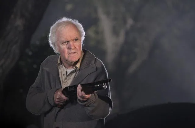 James Handy as an elderly man holding a shotgun, looking distressed.