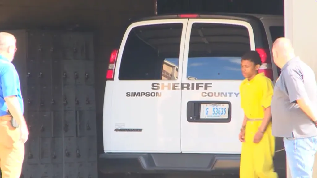Cordarius Laray Hobbs, 17, in a yellow jumpsuit, is escorted by officers in front of a white Simpson County Sheriff's van.