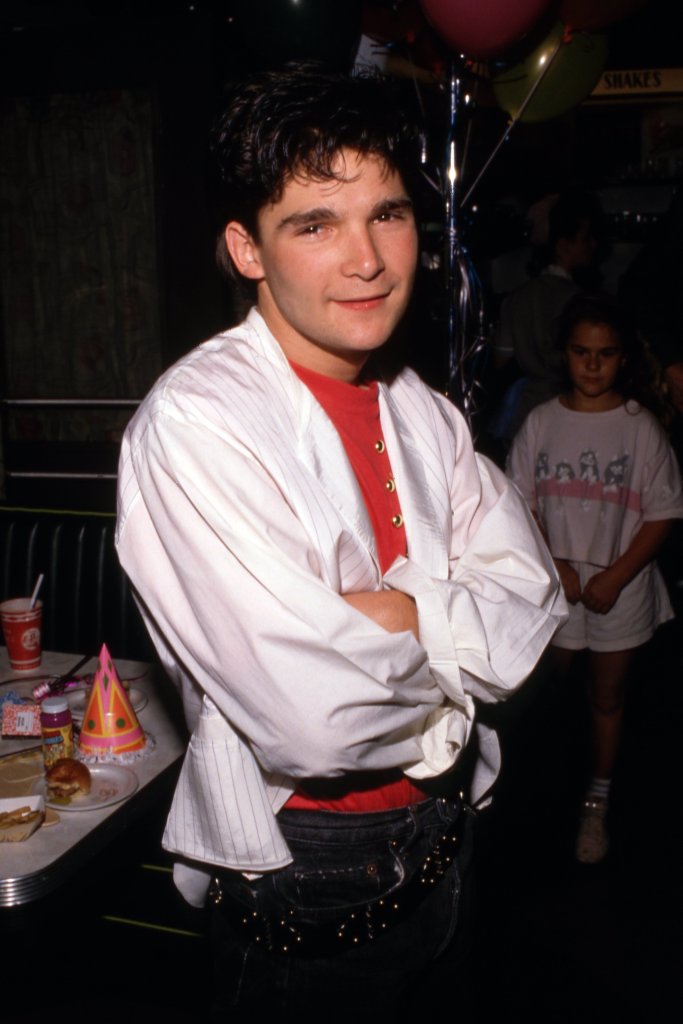 Corey Feldman smiling with his arms crossed at an event.