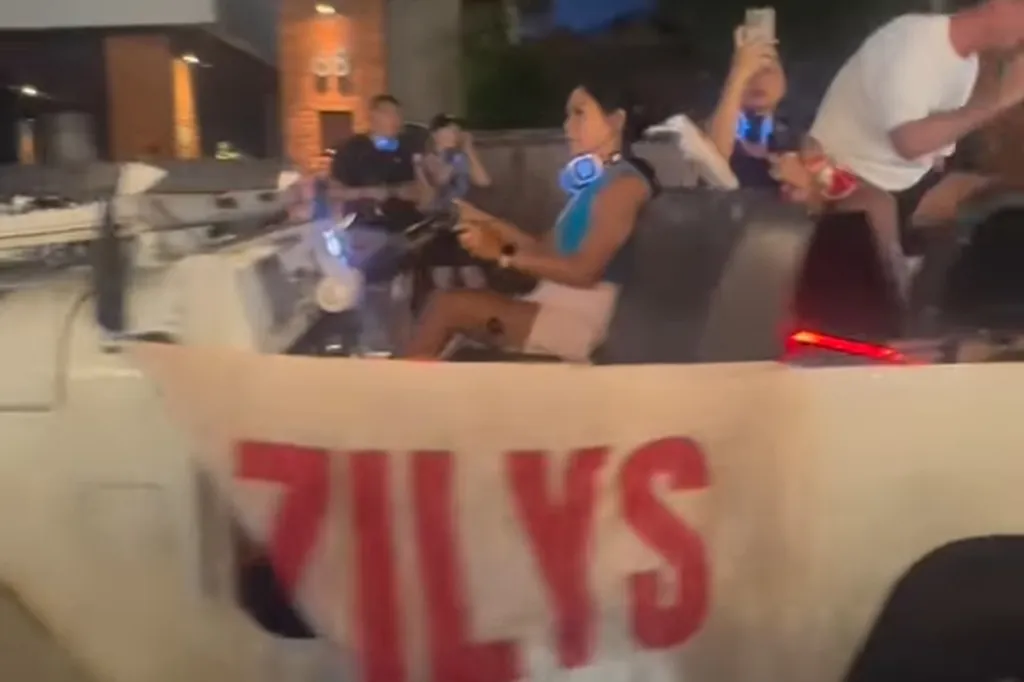 A woman driving a vehicle with a "ZILYS" banner on its side.