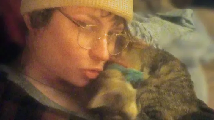 Daveigh Chase wearing glasses and a beanie, holding a tabby cat.