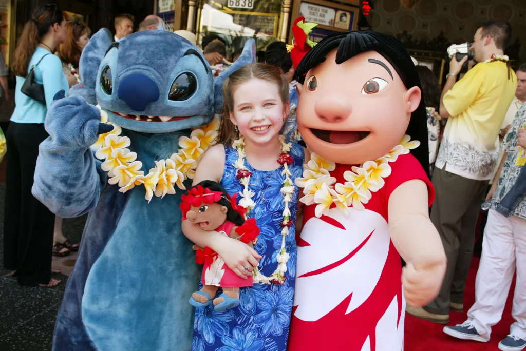Daveigh Chase, the voice of Lilo, smiling between costumed characters Stitch and Lilo at the premiere of "Lilo & Stitch."