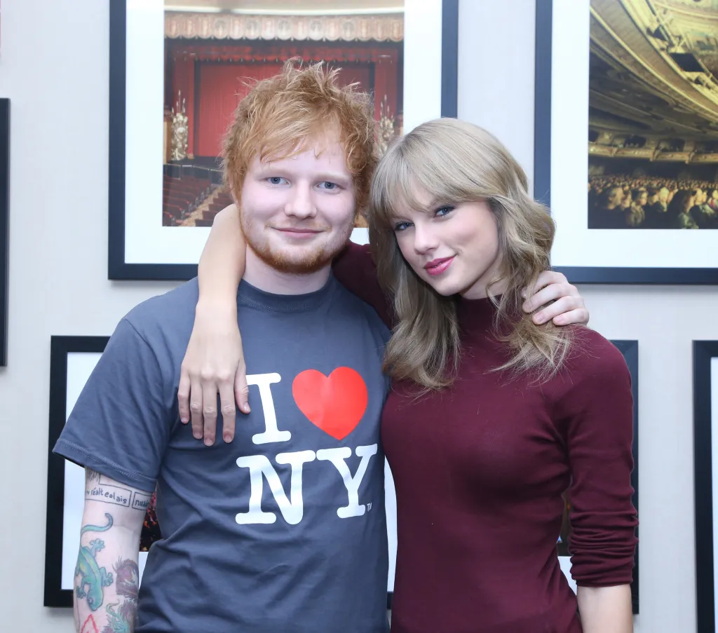 Ed Sheeran in an "I Love NY" shirt and Taylor Swift in a maroon top with her arm around him.