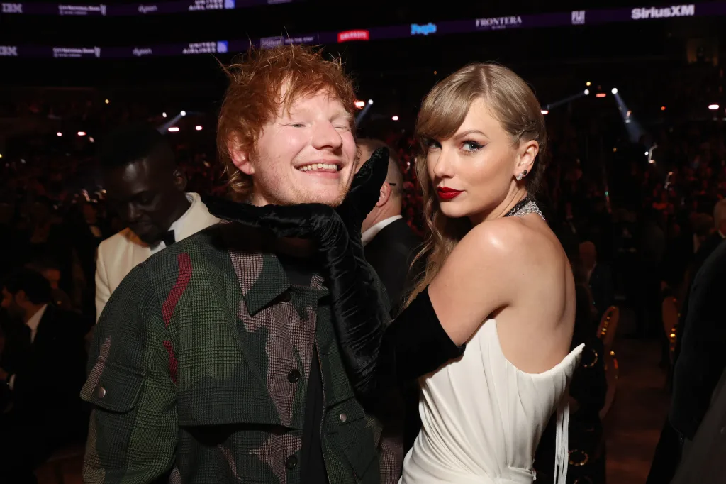 Taylor Swift holding Ed Sheeran's chin while he smiles at the 66th GRAMMY Awards.