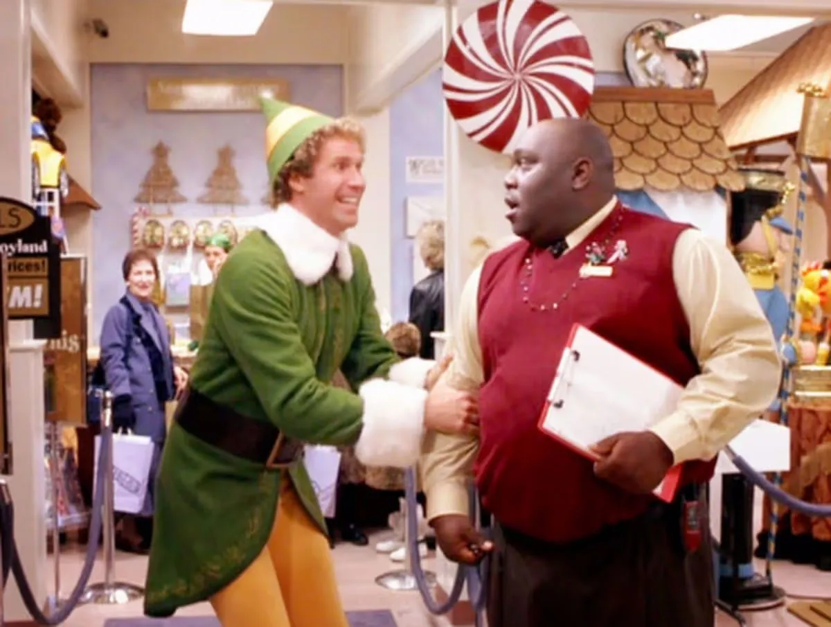 Will Ferrell as Buddy the Elf shaking hands with Faizon Love as Gimbel's manager.
