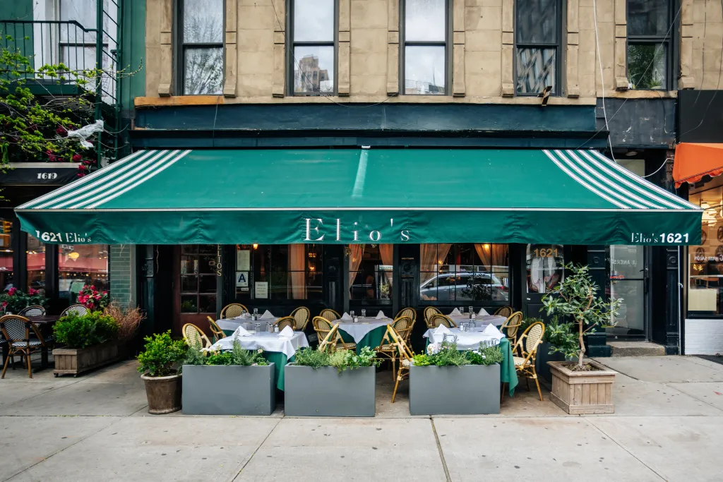Elio's restaurant in the Upper East Side of Manhattan with outdoor dining under a green awning.